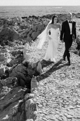 Couple de mariés marchant sur chemin côtier pavé avec vue mer Méditerranée en noir et blanc