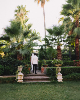 Marié en costume clair marchant dans jardin sicilien avec palmiers et escaliers en pierre