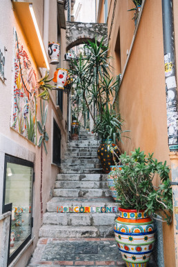 Ruelle sicilienne pittoresque avec escaliers en pierre, pots de céramiques colorées et plantes grimpantes