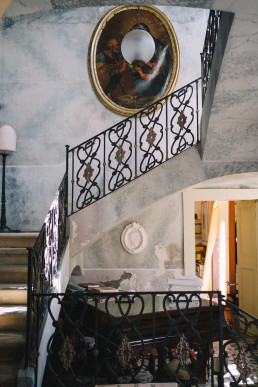 Sicilian Baroque stone staircase with black wrought iron handrail, large oval gilded mirror on the wall and historic palace interior