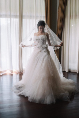 Bride in white tulle gown with veil in front of bright Four Seasons Chiang Mai window