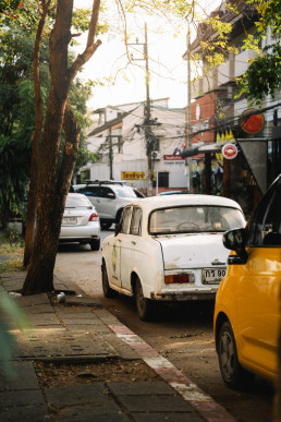Chiang Mai street with vintage white car and yellow tuk-tuk under golden light