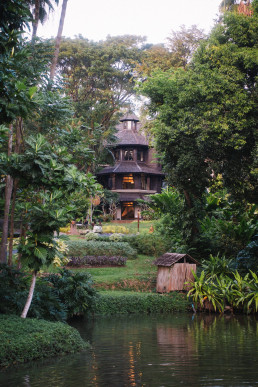 Traditional Thai wooden house illuminated at dusk surrounded by tropical garden and Four Seasons Chiang Mai pond