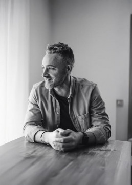 Black and white portrait of the groom seated at a table in natural light