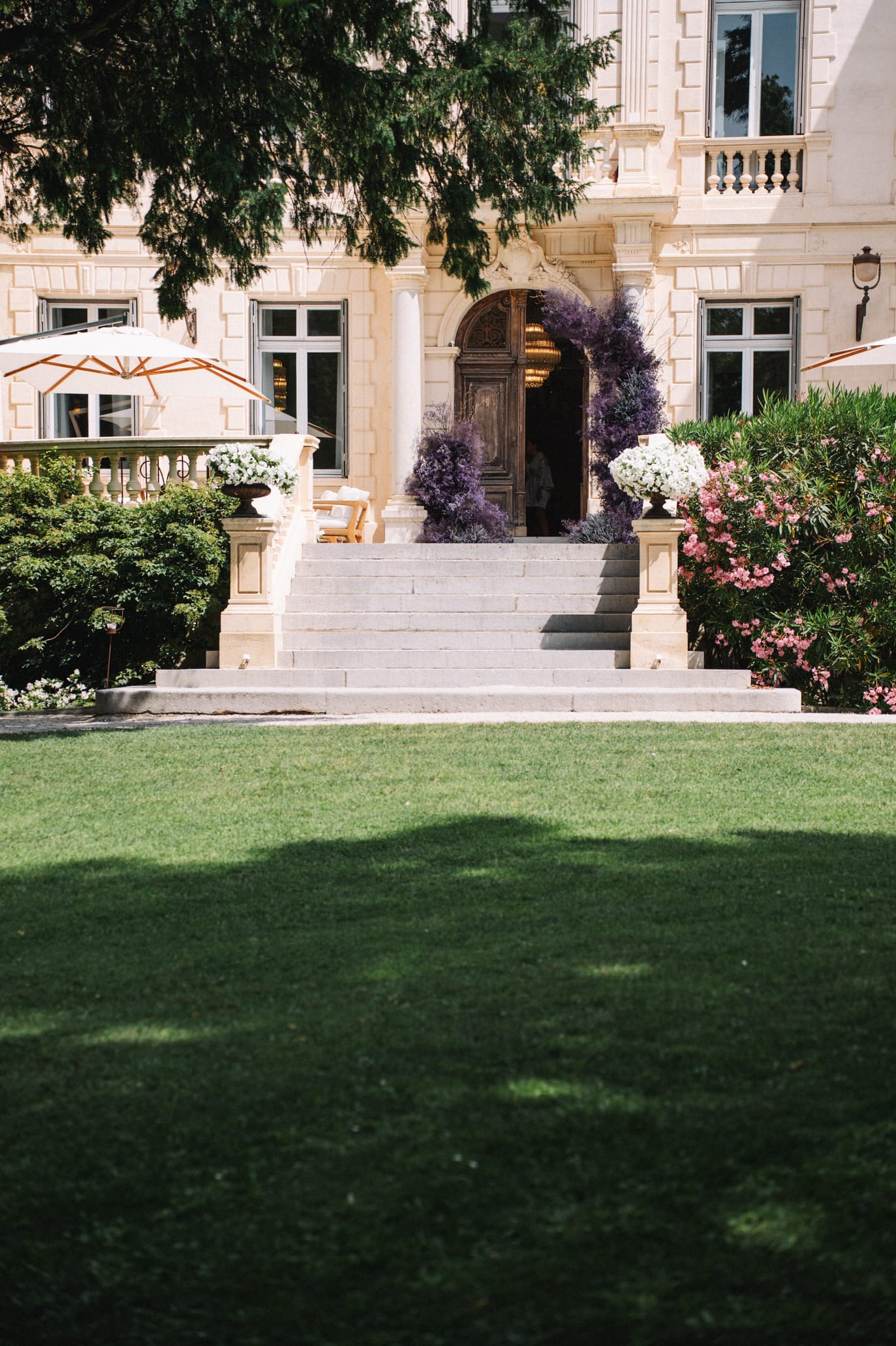 Façade d'un château provençal en pierre ocre avec double escalier courbe central menant à une porte en bois sculpté, pelouse verte et rosiers