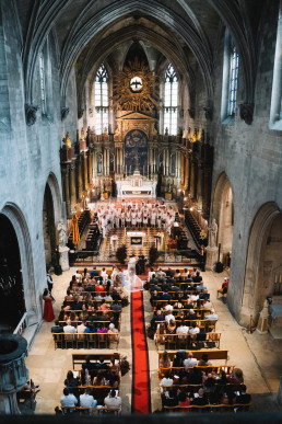 Vue aérienne plongeante de l'intérieur d'une cathédrale gothique pendant une cérémonie de mariage avec voûtes en pierre grise, autel baroque doré illuminé et invités dans les bancs