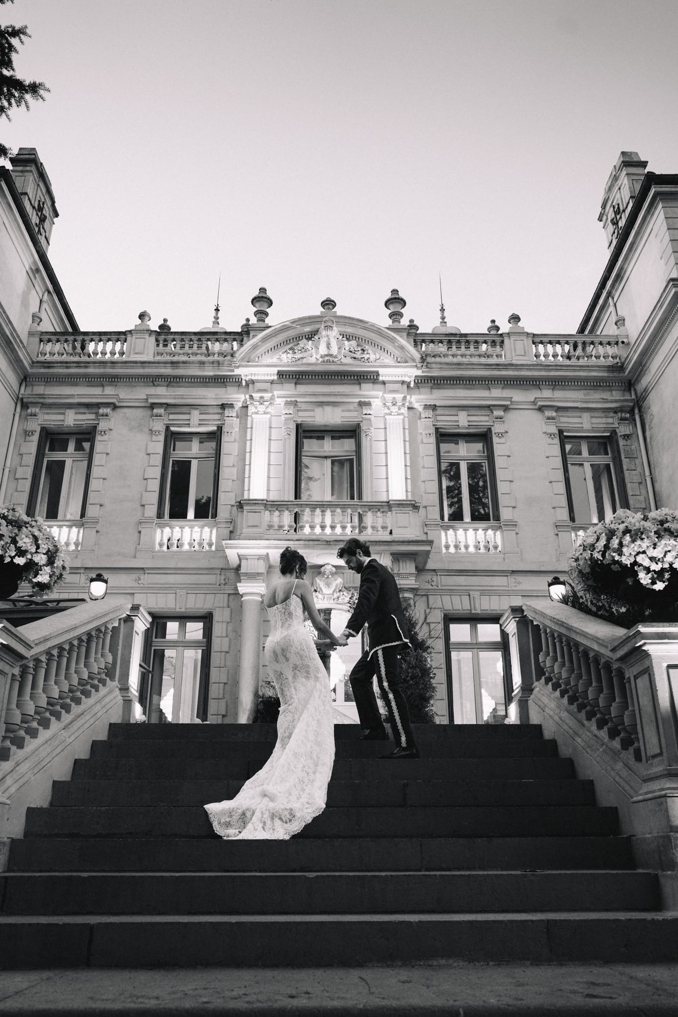 Couple de mariés sur escalier monumental en noir et blanc devant château classique
