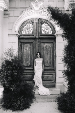 Mariée en robe bustier devant porte ancienne en bois avec ferronneries en noir et blanc