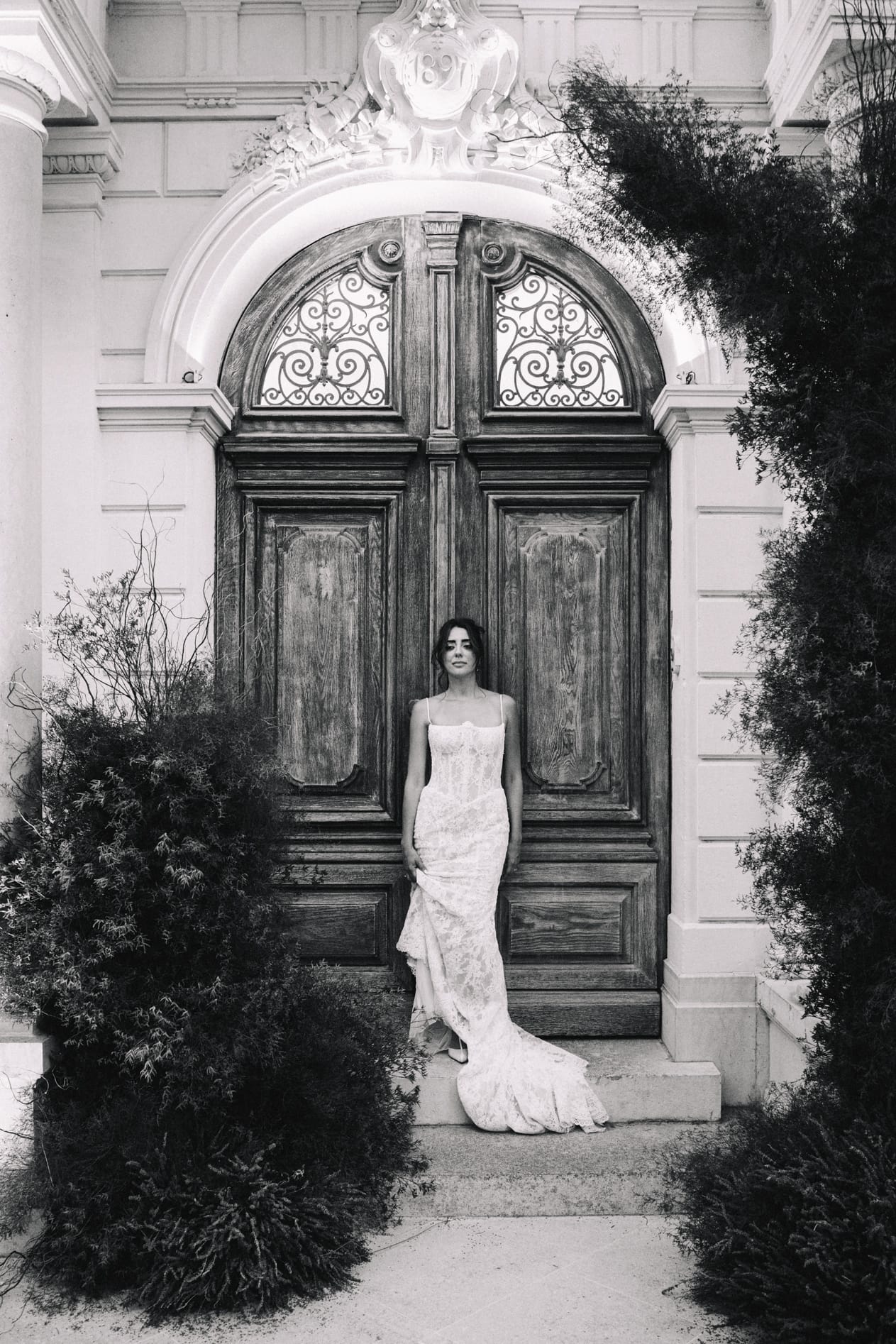 Mariée en robe bustier devant porte ancienne en bois avec ferronneries en noir et blanc