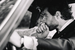 Photo noir et blanc d'un marié en costume embrassant tendrement la main de sa mariée en robe blanche