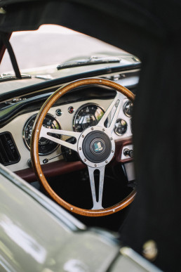 Close-up of the interior of a white classic car with light varnished wood steering wheel, chrome dashboard and vintage meters