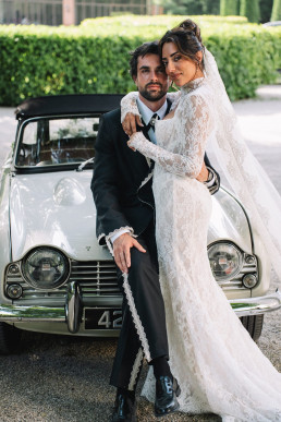 Wedding couple posing with vintage white car in front of trimmed box hedge
