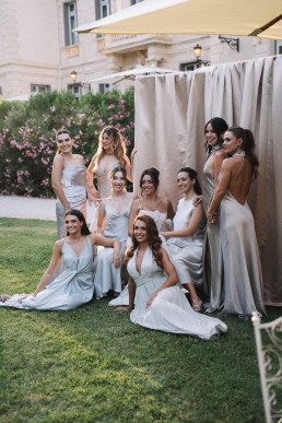 Group of bridesmaids in white and gray dresses, seated and standing in a Provencal château garden.