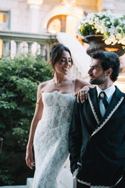 Bride and groom pose in front of a monumental stone vase with a bouquet of white flowers, Provencal architecture with balustrade and greenery.