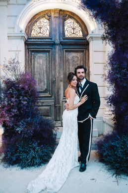 Bride and groom in front of ornamental antique door with lavender-blue garden