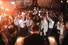 Animated wedding evening with DJ and saxophonist, guests dancing under orange lights