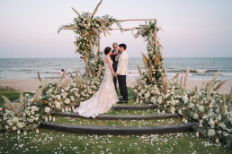 Beachfront wedding arch with couple kissing at sunset in Bali, Indonesia, destination wedding photographer and videographer moment
