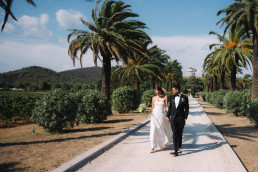 Couple walking under palm trees near beach road in Bali, Indonesia, destination wedding videographer cinematic shot