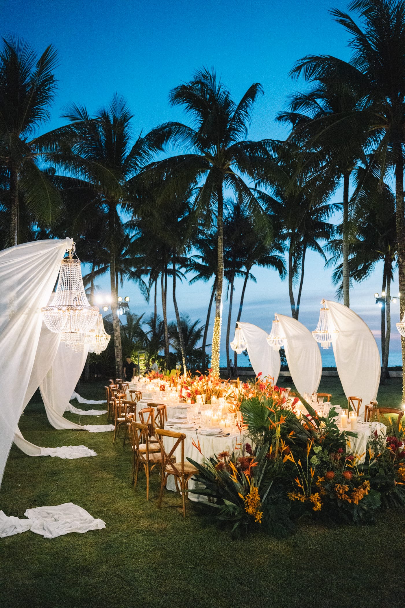Elegant wedding dinner setup under palm trees at sunset on a tropical beach
