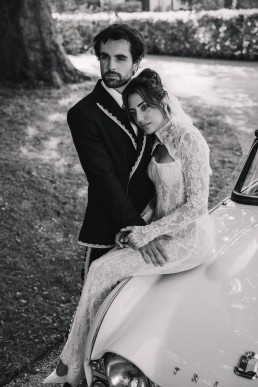 Couple de mariés en noir et blanc près d’une voiture vintage