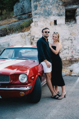 Destination wedding couple beside a vintage car during a coastal road trip