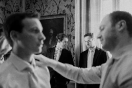 Black-and-white photograph of groomsmen helping the groom with his tie at Château Valmousse