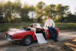 Bride and groom relaxing beside a red vintage convertible after their ceremony at Château Valmousse