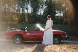 Bride standing beside a red vintage convertible on her wedding day at Château Valmousse