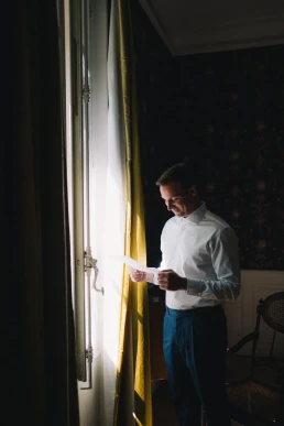 Groom reading a letter by the window before his wedding at Château Valmousse