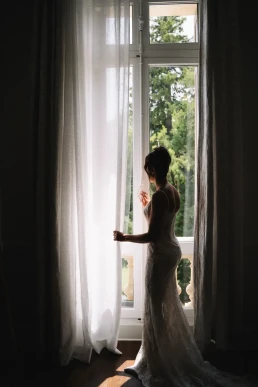 Silhouette of a bride looking through a tall window before her wedding in Scotland