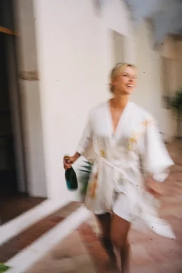 Bride in a silk robe carrying champagne during her elopement preparations in Tuscany, Italy