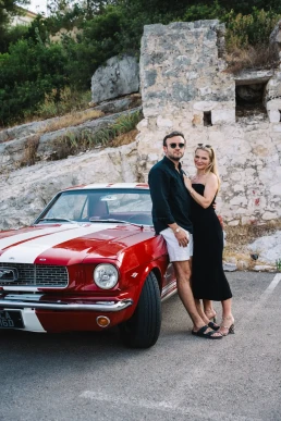 Bride and groom beside a vintage red car during a destination wedding weekend